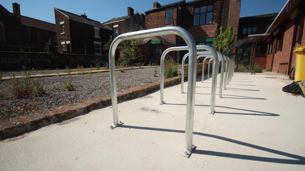 Traditional Sheffield Bike Stands lined up next to each other, bolted securely to the ground with overground fixings. These stands are newly installed and in an outdoor space. 