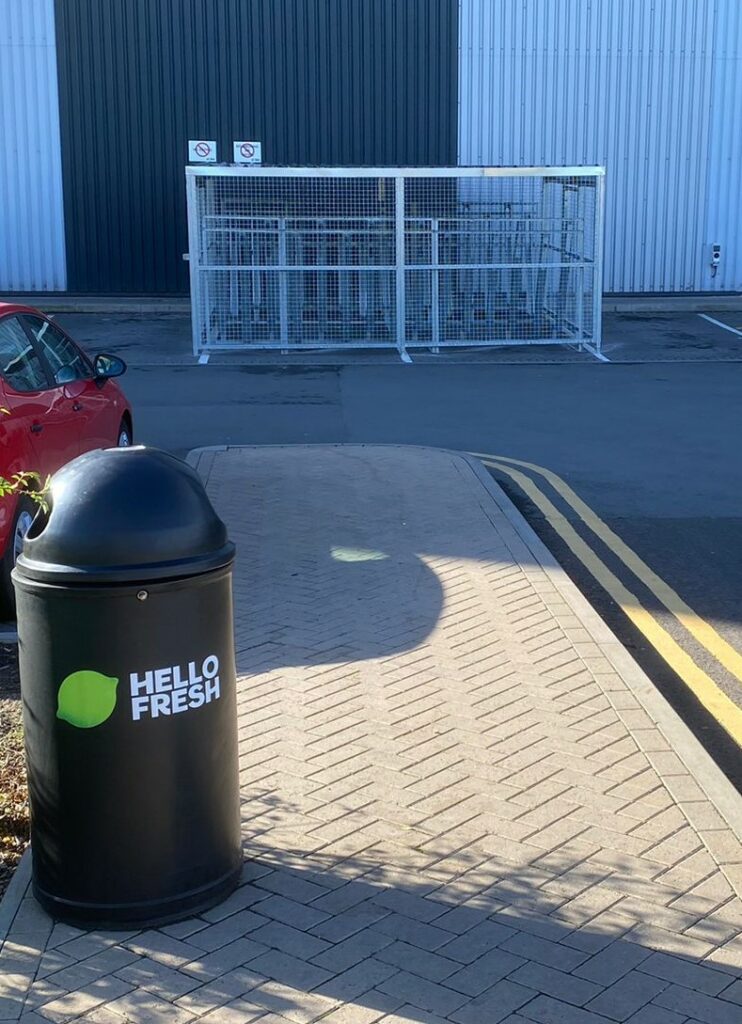 newly installed merton mesh bike shelter, located outdoors behind hello fresh bin.