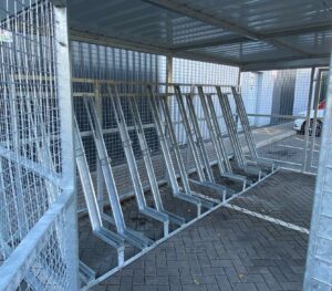 newly installed merton mesh bike shelter with semi-vertical bike racks, located outdoors behind hello fresh bin.